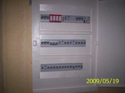 Otwarta skrzynka elektryczna z trzema rzędami zabezpieczeń, widoczne ograniczniki przepięć i wyłączniki, data wykonania zdjęcia w prawym dolnym rogu.